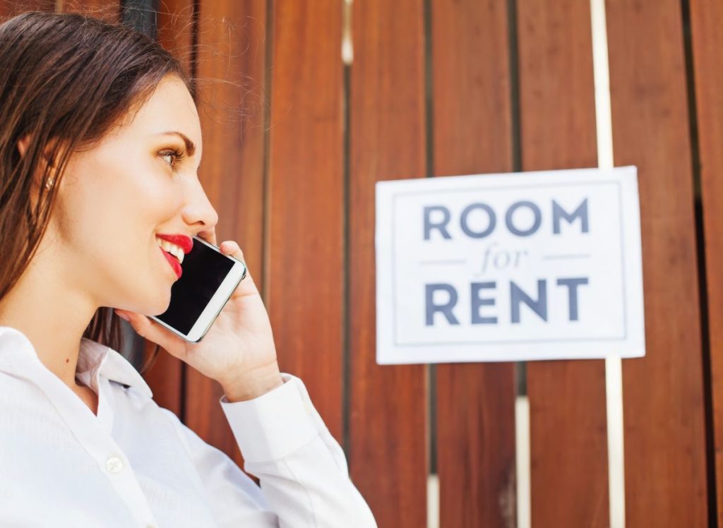 A young lady speaking on her mobile phone in front of a room for rent sign