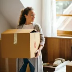 Woman smiling while holding a cardboard box in her bedroom