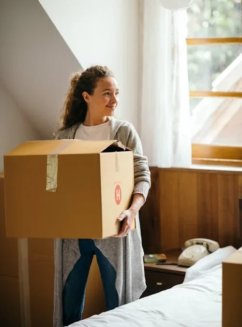 Woman smiling while holding a cardboard box in her bedroom