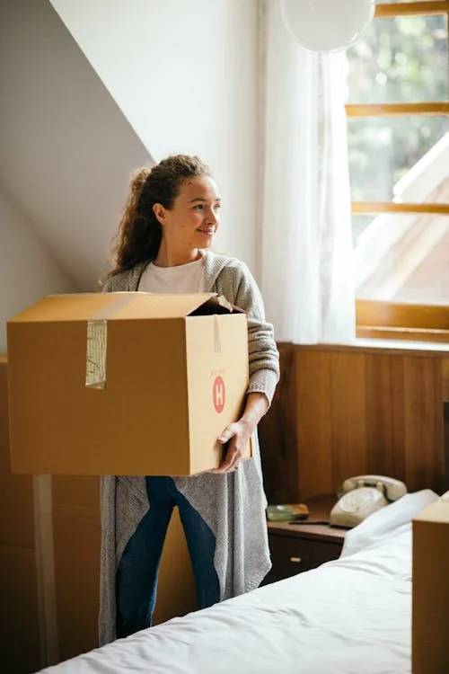 Woman smiling while holding a cardboard box in her bedroom