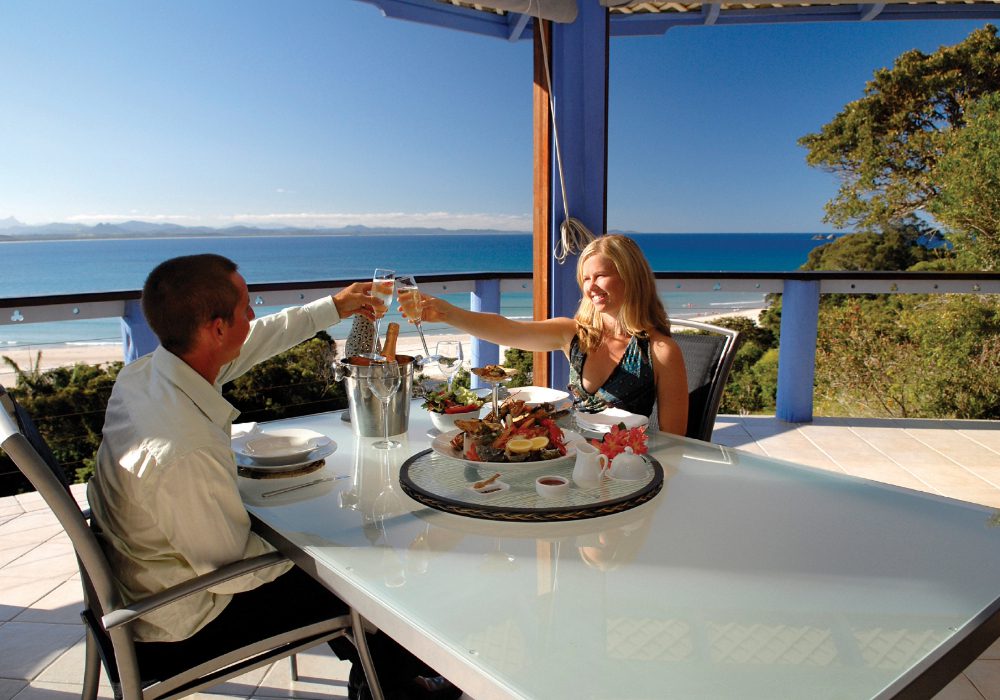 A couple toasting drinks and having food by the beach in Australia